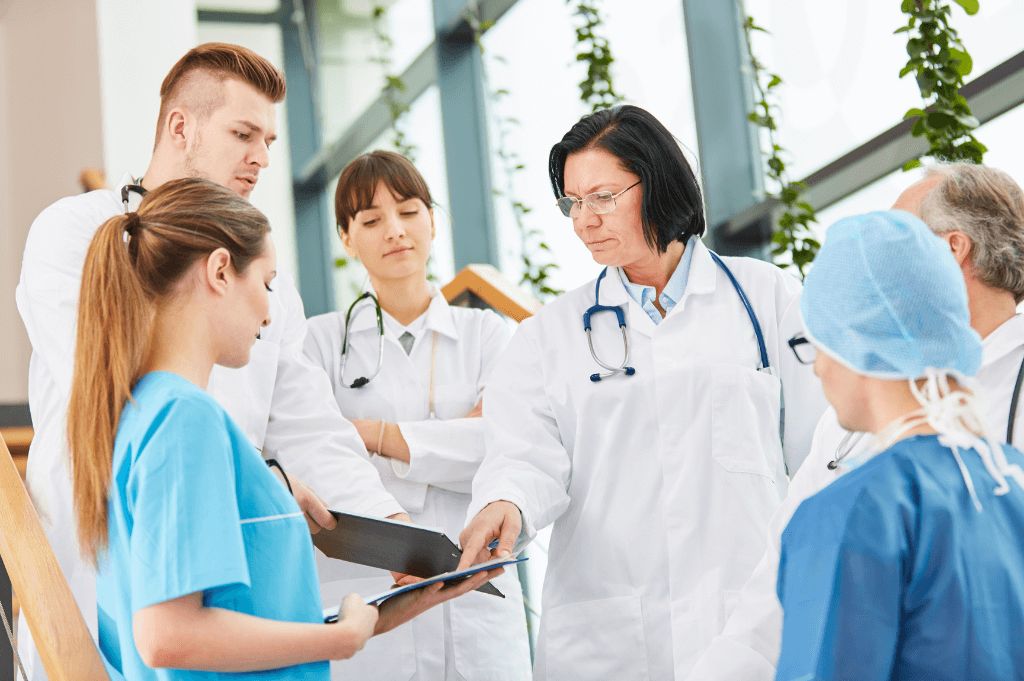 Doctors in white coats giving training to residents in scrubs.