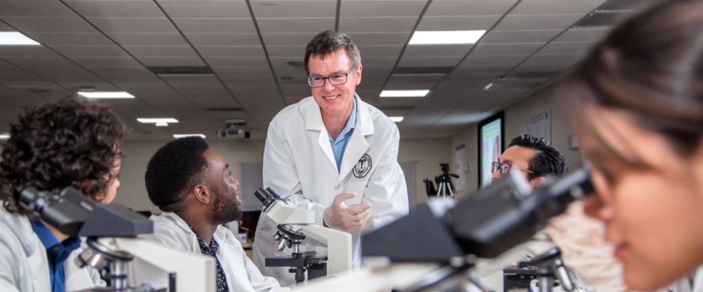 Male faculty member teaching a class with microscopes